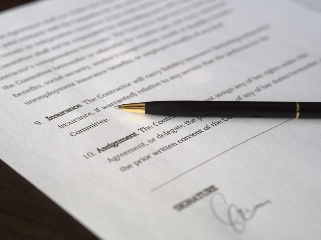 A imagem mostra uma folha sulfite que aparenta ser um contrato, escrito em inglês. Sobre ela há uma caneta preta com detalhes dourados. 