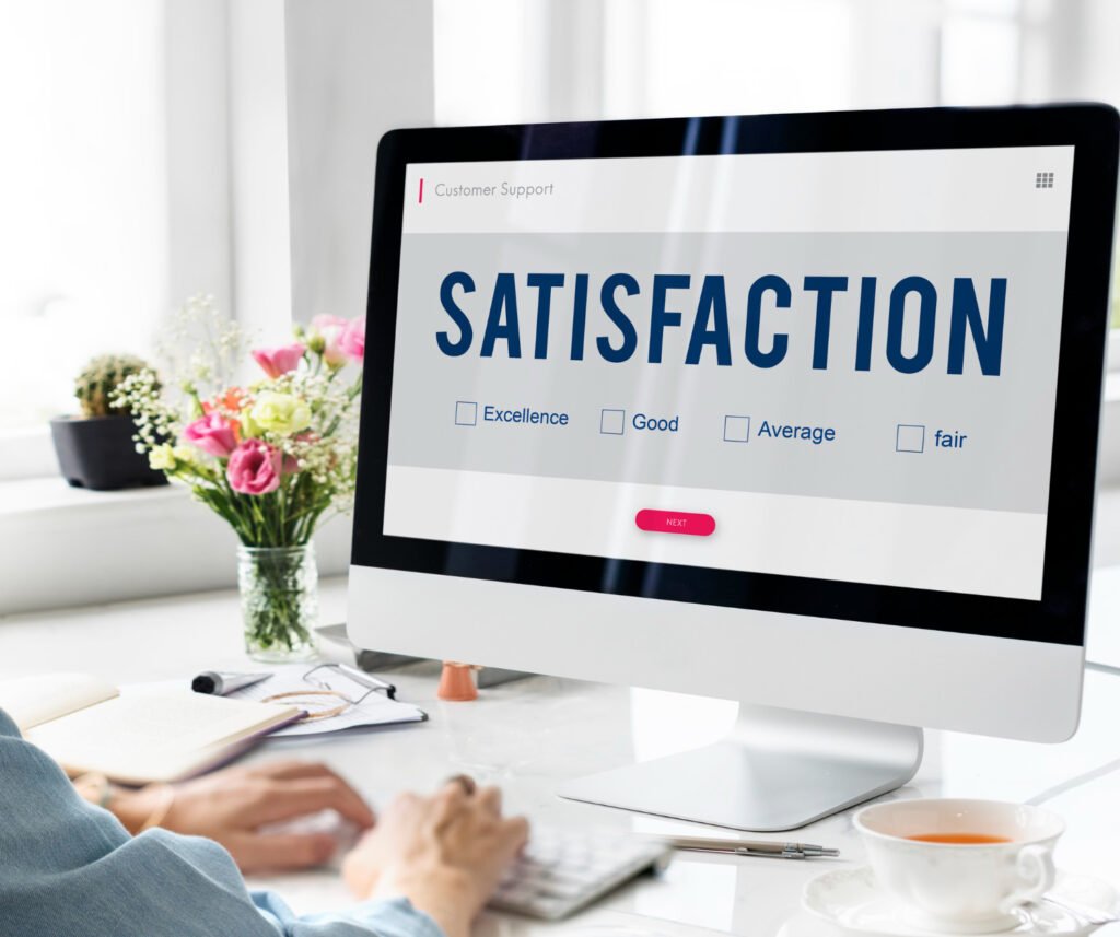 O monitor de um MacBook aparece sobre uma mesa branca. Na tela dele é possível ler “Satisfaction” em letras grandes. Abaixo, há algumas caixas de seleção com as opções: “Excellence”; “Good”; “Average”; “Fair”.