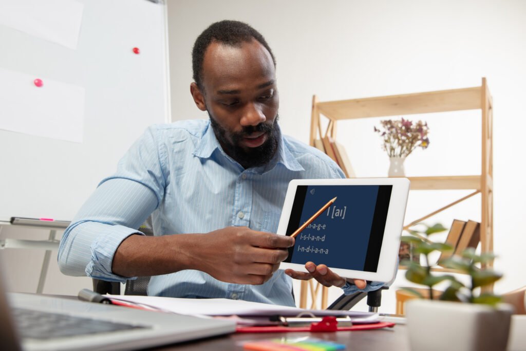 Homem negro segurando um tablet e um lápis ensinando inglês.