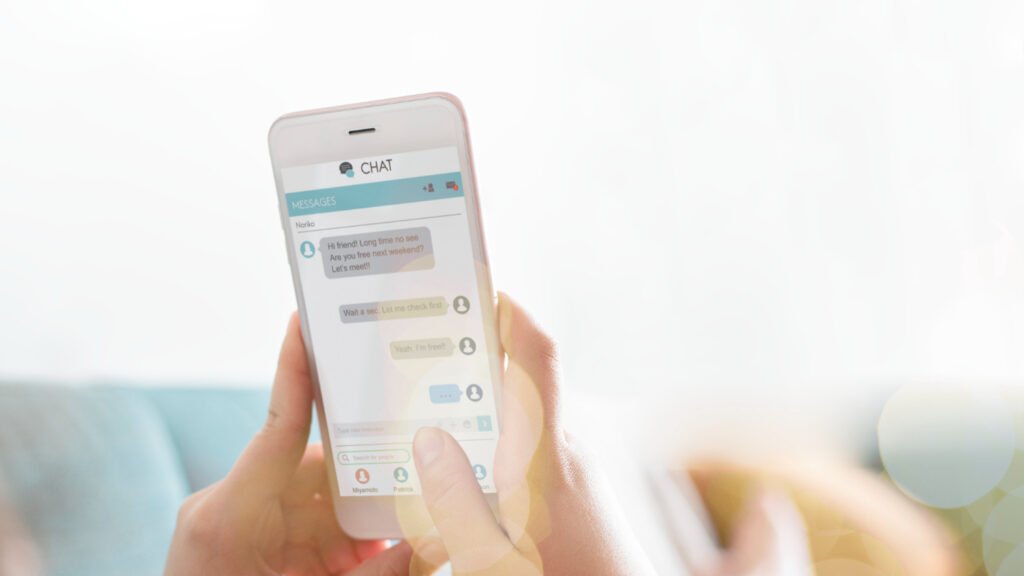 Las manos de una persona blanca sostienen un teléfono móvil. En la pantalla del dispositivo es posible ver una conversación en un chat.