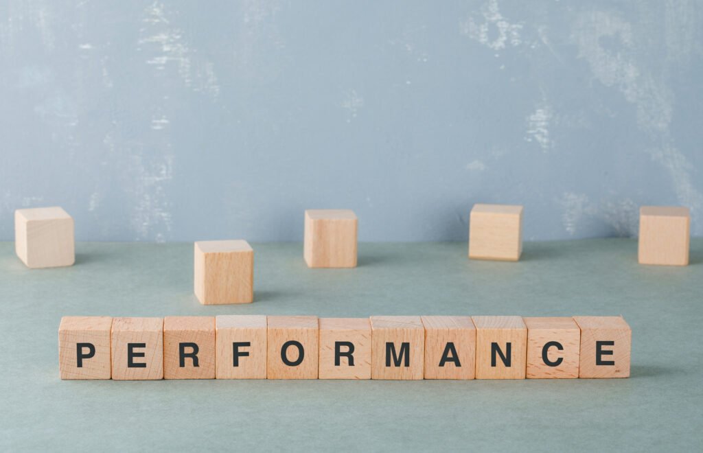 A imagem mostra vários blocos de madeira enfileirados, cada um contém uma letra da palavra performance. Ela representa o fato de a performance ser o foco em avaliações de desempenho.