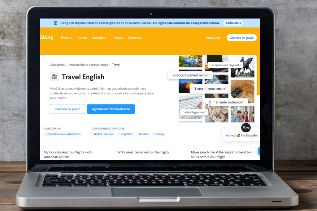 Laptop mostrando a página de “Travel English” no site da Slang, apoiado em uma mesa de madeira com um fundo cinza.