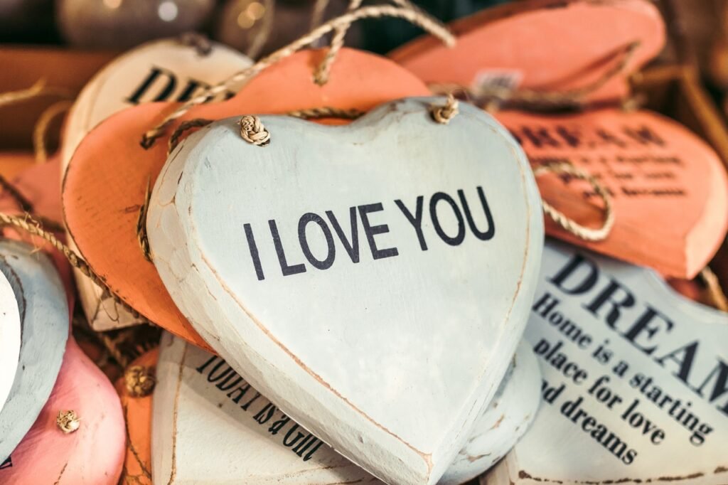 Várias tábuas decorativas em formato de coração nas cores branco e laranja, com frases escritas. O coração em destaque carrega a frase “I love you”.