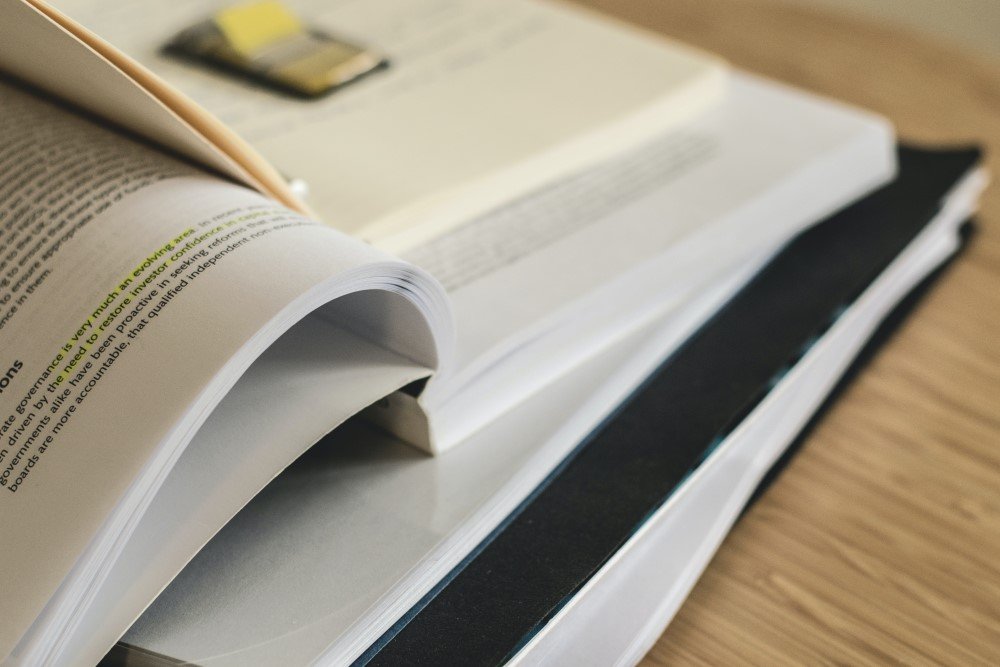 Livros abertos e empilhados sobre uma mesa de madeira.