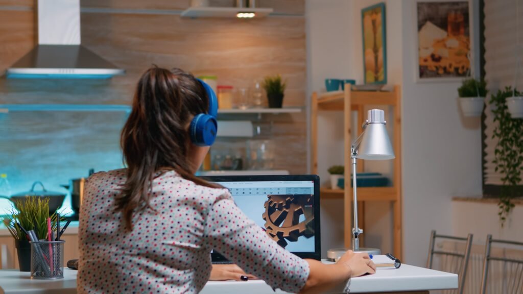 Mulher usando headphones azuis sentada de costas mexendo em um laptop.